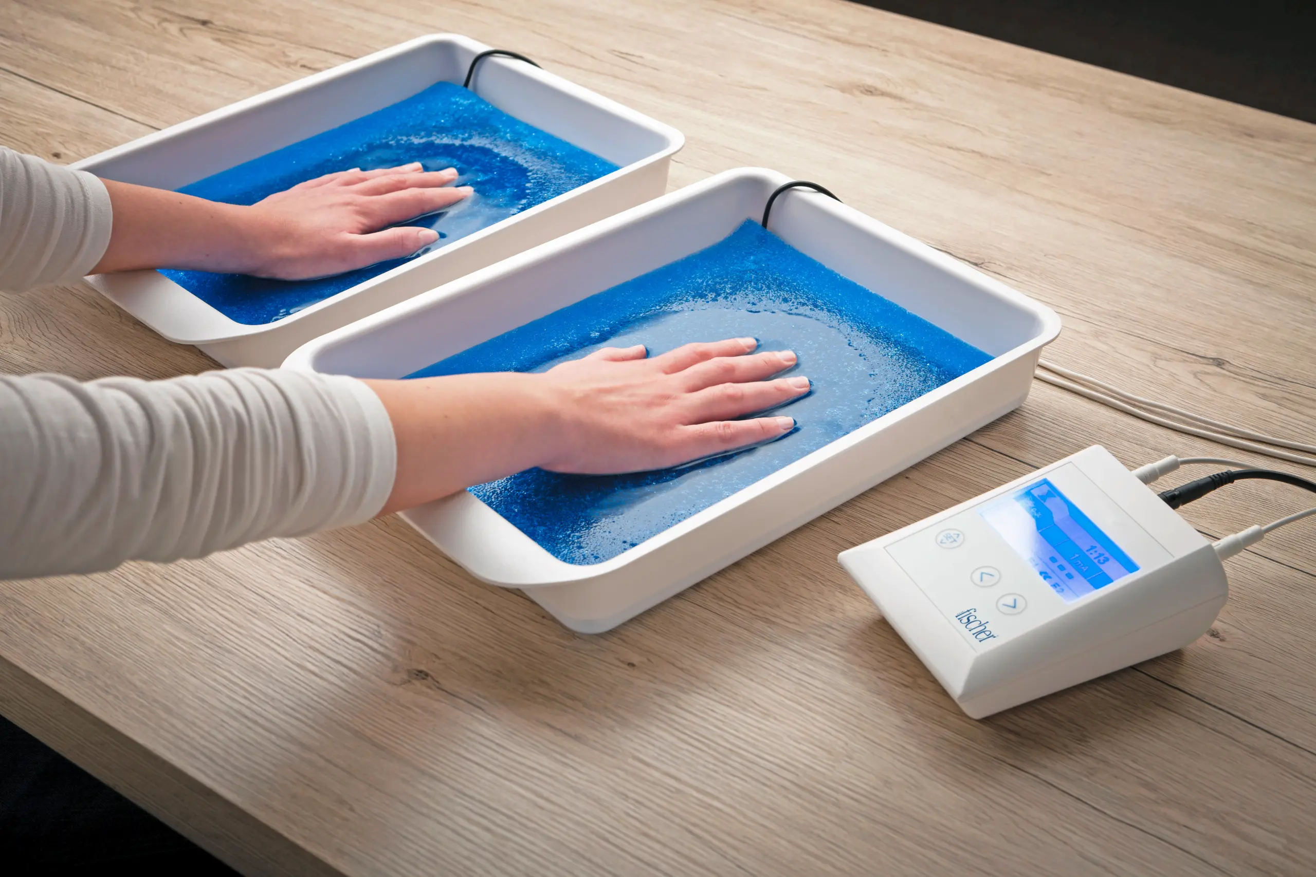 Photograph of a person treating their palmar hyperhidrosis using RA Fischer Co.'s The Fischer iontophoresis device on a wooden table.