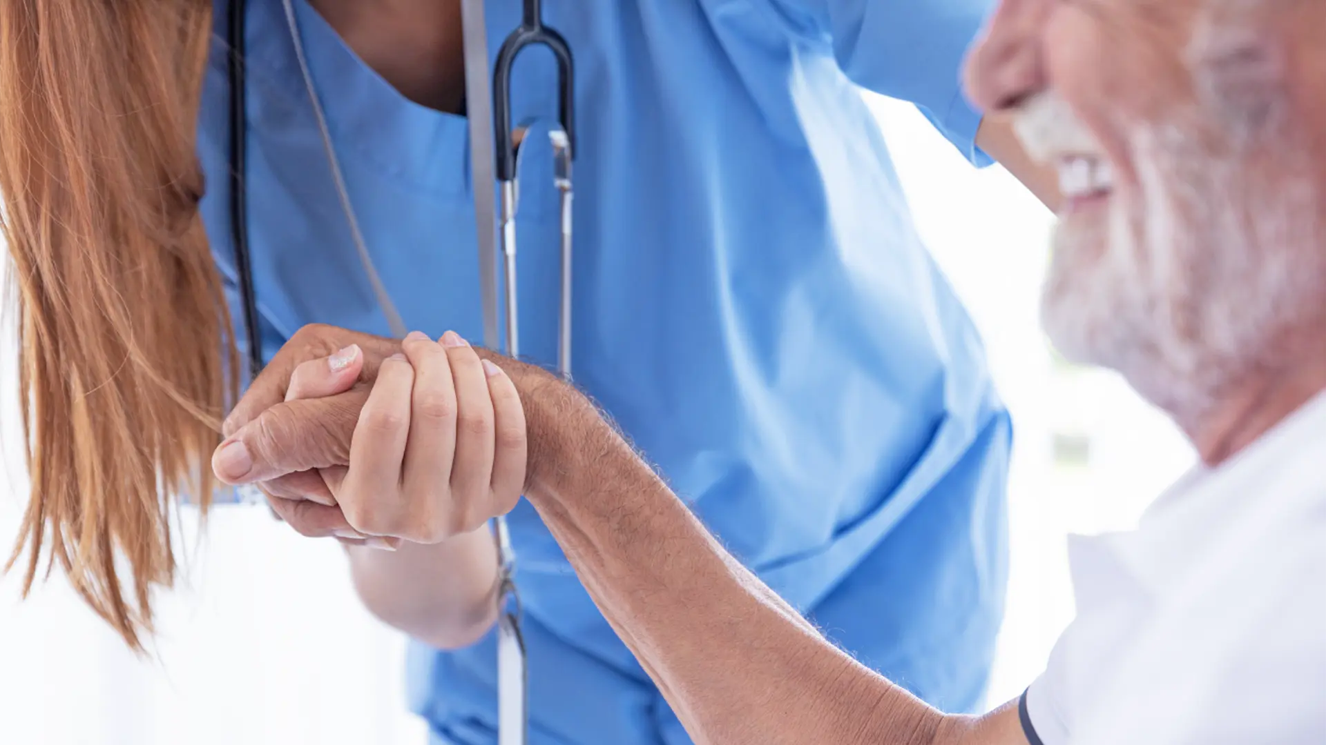 A caring nurse providing comfort to an elderly man by holding his hand.