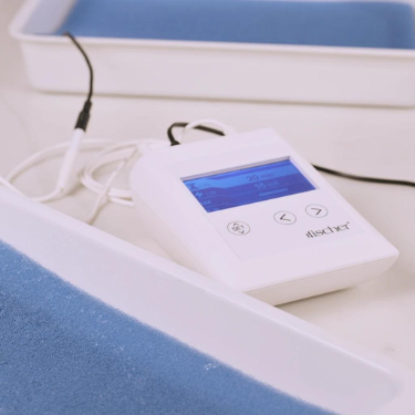 Image of the Fischer control unit next to the Fischer water bath trays. The Fischer is white with a blue screen lit up. The trays are white and the pH-balancing foam is blue and inside the trays.