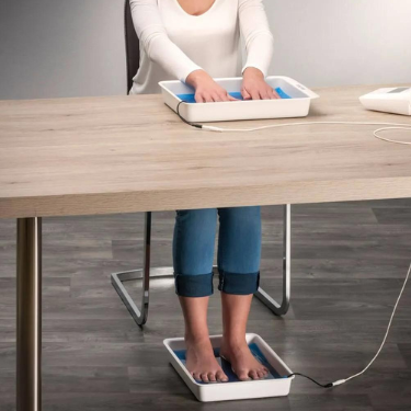 A lady in a white blouse and denim pants immerses her hands and feet into the Fischer iontophoresis device water bath trays to address palmar hyperhidrosis (excessive hand sweating) and plantar hyperhidrosis (excessive foot sweating). The Fischer iontophoresis device from RA Fischer Co. allows simultaneous treatment of both hands and feet.