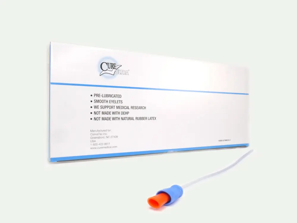 Picture of a box of Cure Ultra pre-lubricated catheters from RA Fischer. In front of the box is one of the catheters with an orange and blue gripper. Box reads "CURE ULTRA" "PRE-LUBRICATED" SMOOTH EYELETS" WE SUPPORT MEDICAL RESEARCH" "NOT MADE WITH DEHP" "NOT MADE WITH NATURAL RUBBER LATEX"