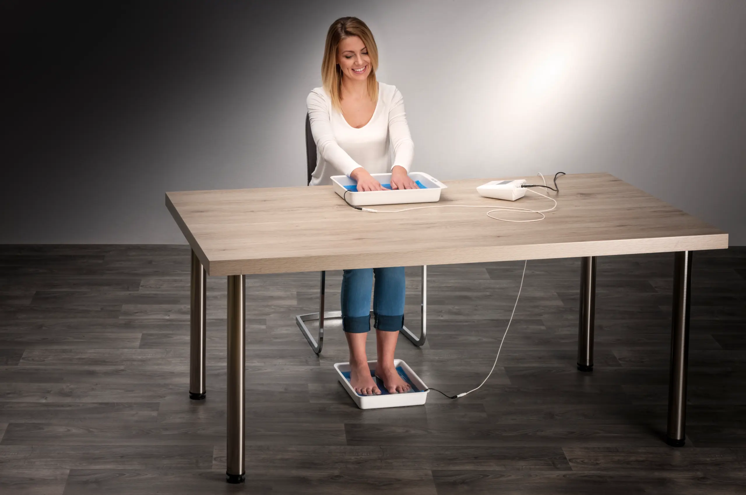 In this scene, we observe a woman elegantly attired in a white blouse and comfortably clad in jeans as she gracefully immerses her hands and feet into the water bath trays of the Fischer iontophoresis device, thoughtfully designed to offer relief from the burdensome challenges of palmar hyperhidrosis (excessive hand sweating) and plantar hyperhidrosis (excessive foot sweating). The Fischer iontophoresis device, proudly crafted by RA Fischer Co., stands out as an innovative solution, as it seamlessly allows for the concurrent treatment of both hands and feet, underscoring its effectiveness and convenience in addressing these perspiration-related concerns. This cutting-edge technology represents a significant step towards enhancing the quality of life for individuals dealing with hyperhidrosis.