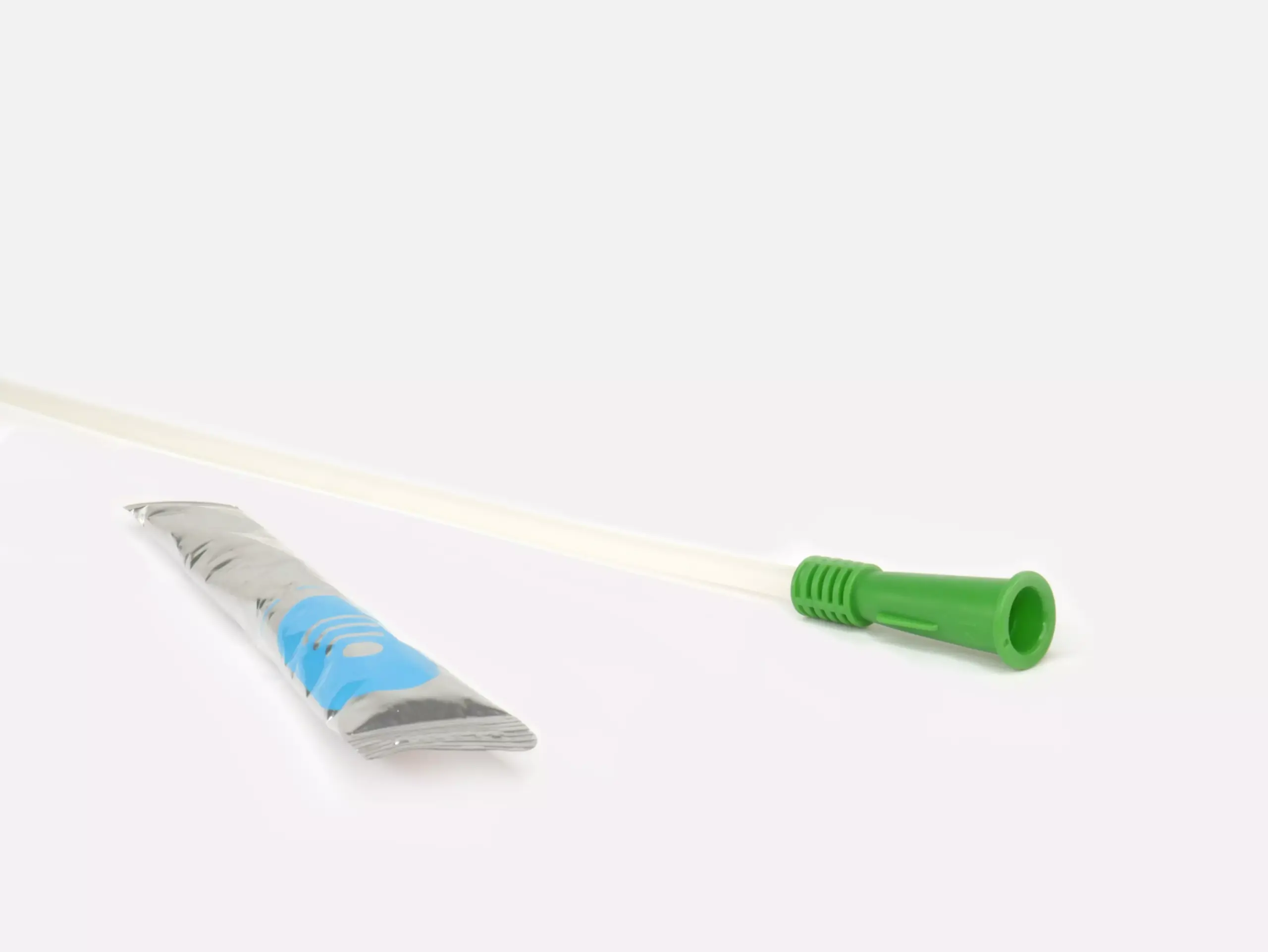 Photograph of a RA Fischer Co. Cure brand catheter with a green grip, positioned next to a silver-colored water packet, against a white background. [ Personalized urology care ]