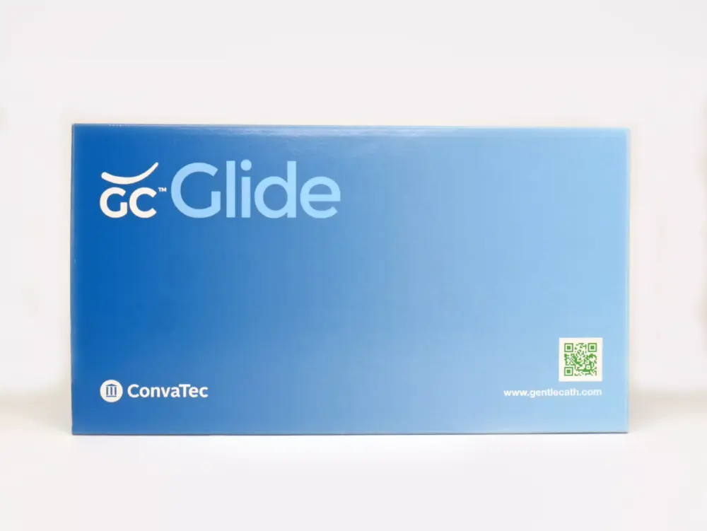 A photograph presenting a carton containing 30 GentleCath Glide (GC GLIDE) catheters, a product of RA Fischer. Placed in front of the box is a catheter with an orange gripper, accompanied by a packet of lubrication or water. The box is marked with "GC Glide," "Convatec," "www.gentlecath.com," and includes a QR code.