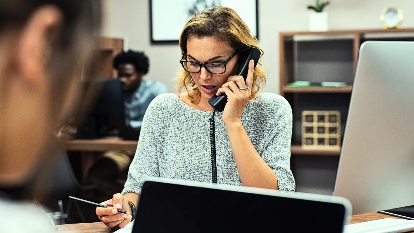 A woman sitting at a desk, engaged in a phone conversation. [contact healthcare treatment specialists] [Treatment specialist consultation]