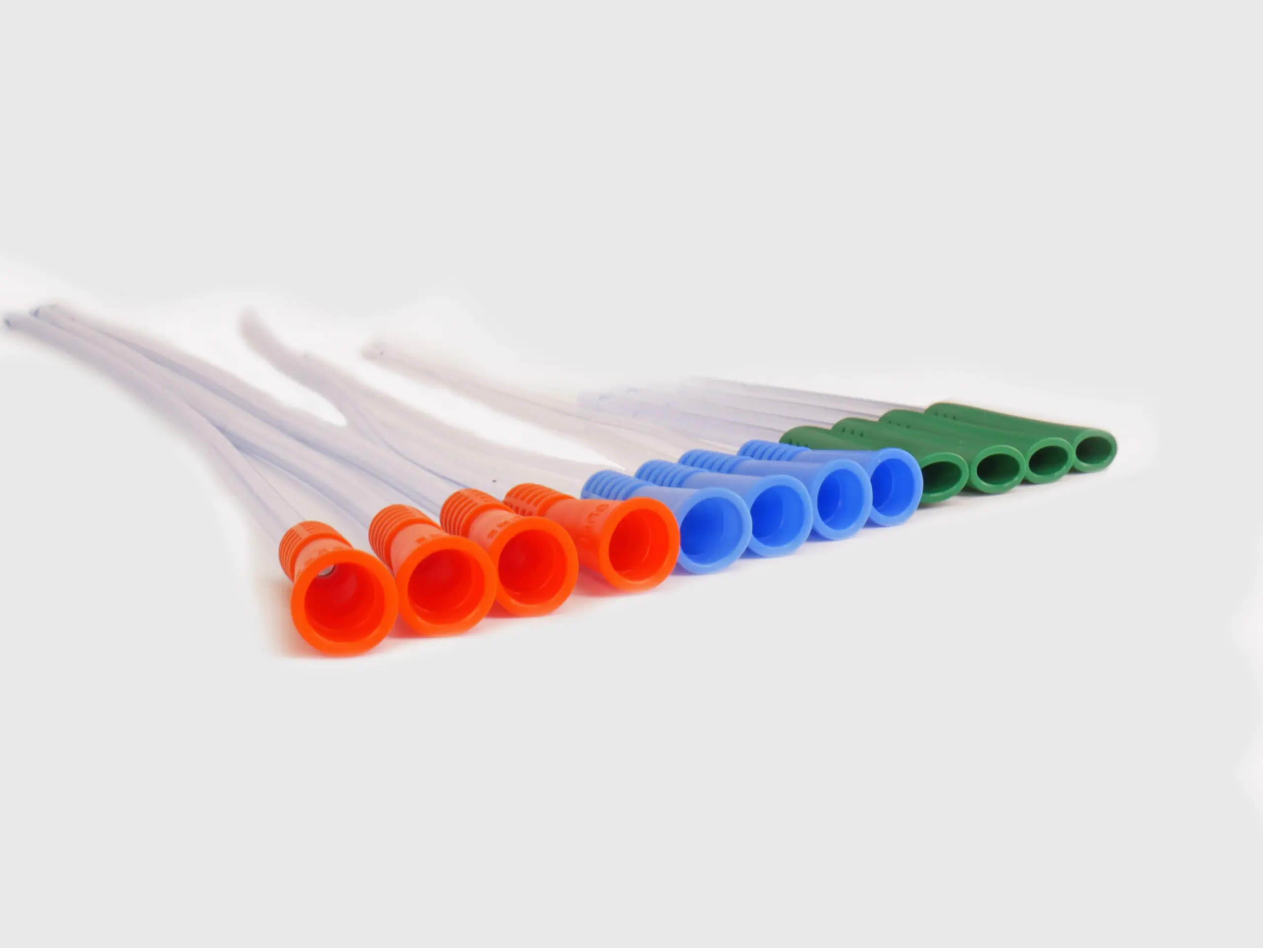 Photograph of an assortment of twelve RA Fischer Co. catheters of deferring lengths and gripper sleeve colors. The catheters are lined up. Grippers are facing camera. Gripper colors are blue green orange. White background [ Personalized urology care ]