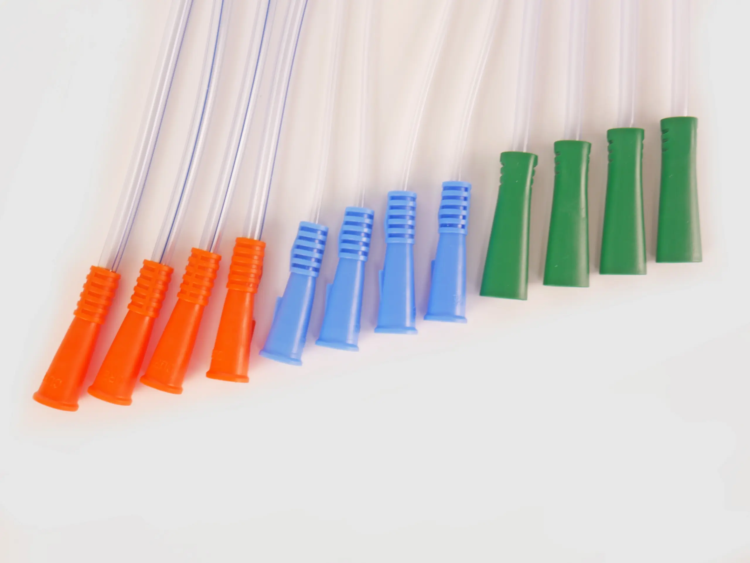 Photograph of an assortment of twelve RA Fischer Co. catheters of deferring lengths and gripper sleeve colors. The catheters are lined up. Gripper colors are blue green orange. White background