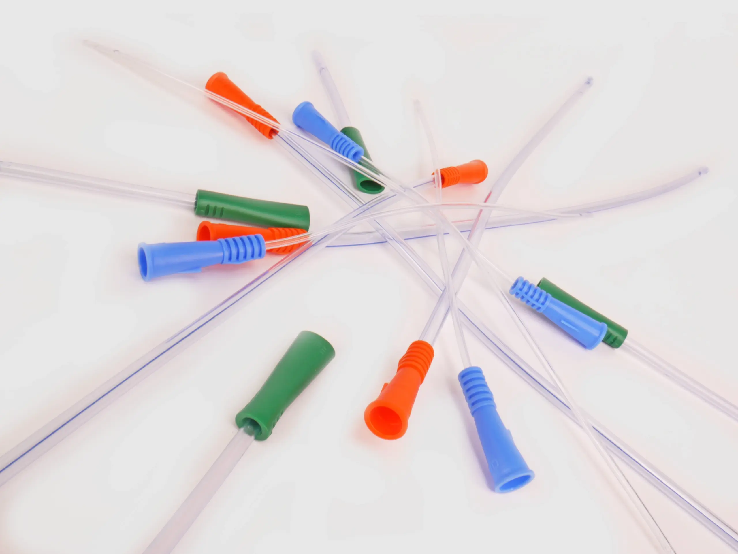 Photograph of an assortment of around twelve RA Fischer Co. catheters of deferring lengths and gripper sleeve colors. Colors are blue green orange. White background
