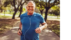 Photograph of an older man jogging through the park, smiling, with a pair of headphones in his ears