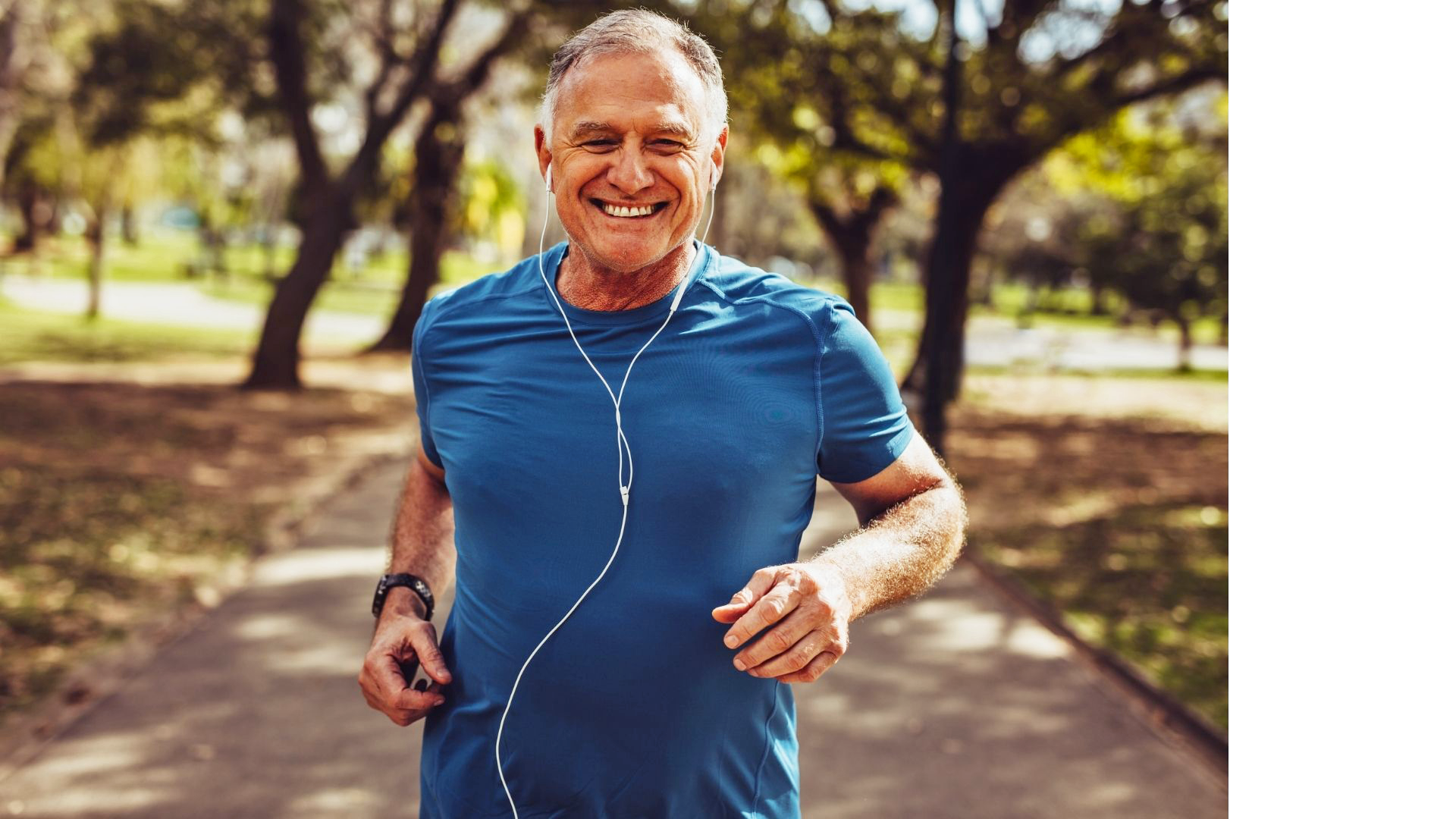 Photograph of an older man jogging through the park, smiling, with a pair of headphones in his ears