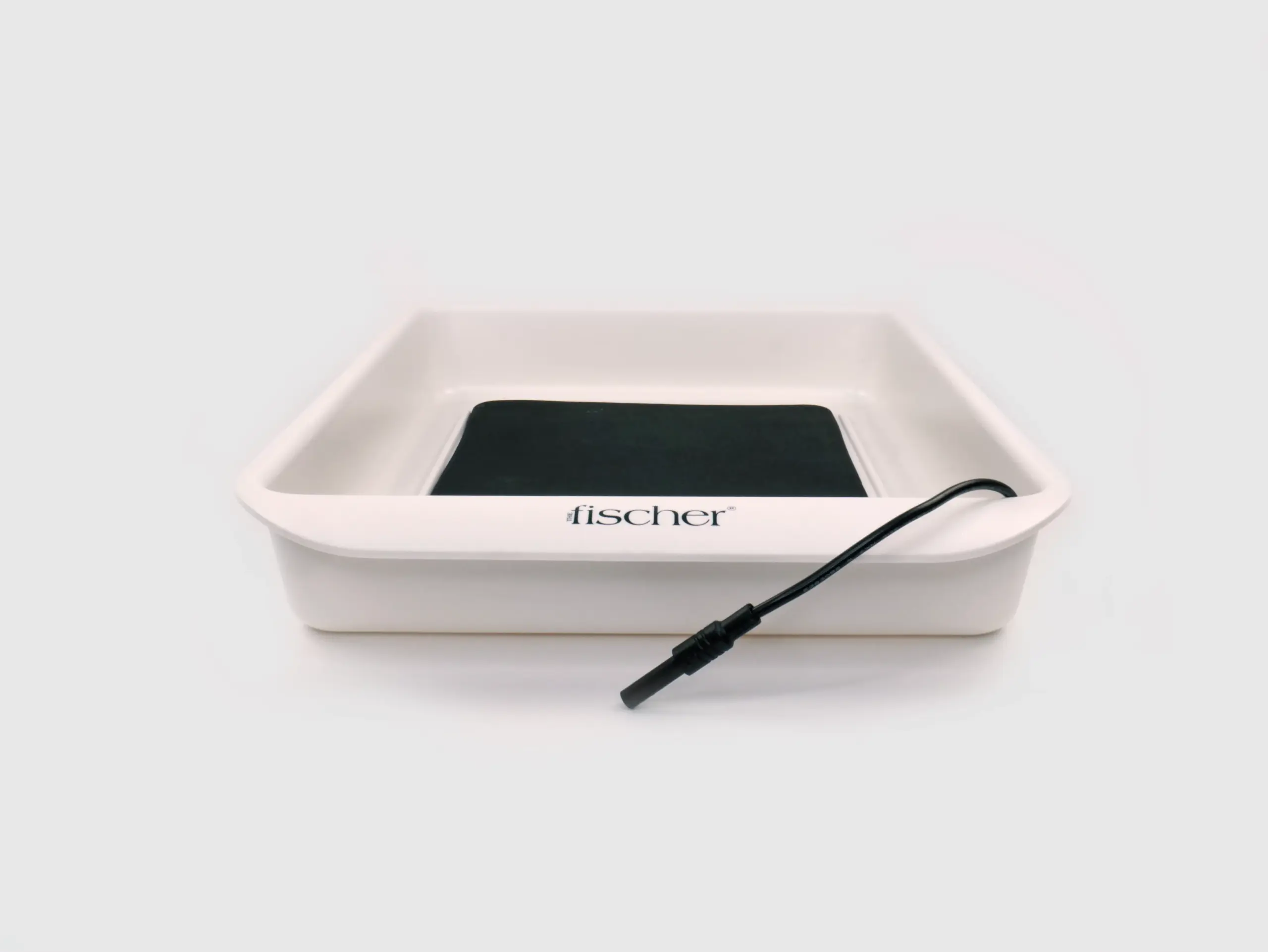 Photograph that precisely spotlights one of the white water bath trays and the black, metal-free silicone electrode contained within RA Fischer's 'The Fischer' Device—an iontophoresis device meticulously designed for the treatment of hyperhidrosis (excessive sweating). The electrode is positioned inside the tray, and the entire composition is set against a clean white background. [ Iontophoresis Device for Sweating ]