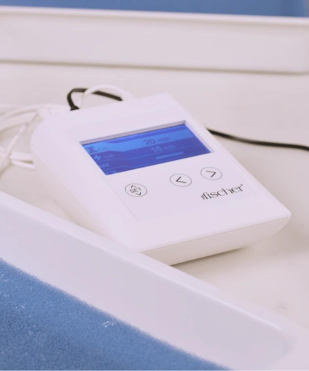 An image showcasing the Fischer control unit alongside the Fischer water bath trays from RA Fischer Co. The control unit boasts a white exterior with a glowing blue screen, while the trays themselves are also white, housing blue pH-balancing foam.