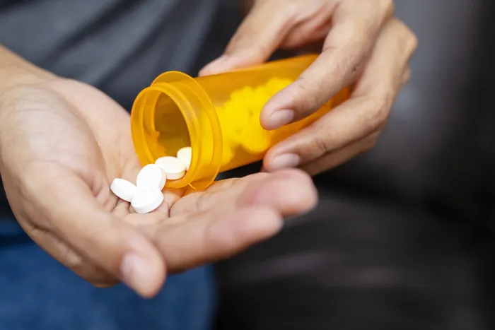 Photograph of a person holding a yellow pill bottle with a white pills inside. Contains medication for oral consumption.