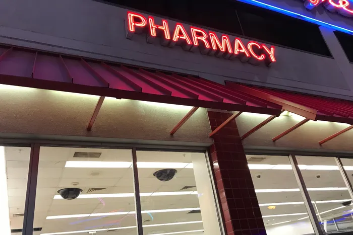 Photograph of a building with a red awning and a neon sign that says 'pharmacy', representing a pharmacy store.